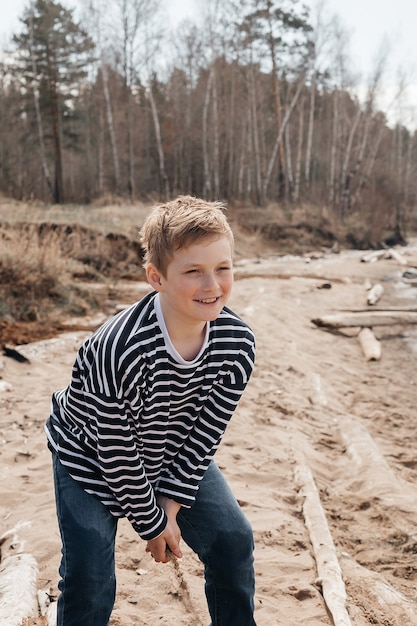 화창한 날 모래를 손에 들고 호수 앞에 서 있는 금발 머리를 한 10세 백인 소년의 초상화. 레크리에이션 국내 관광.