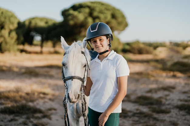 Portrait of 12 year old girl standing with helmet posing next to her white pony