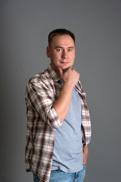 Portrait of a 30s man in casual clothes holding his hand on his chin on a gray background