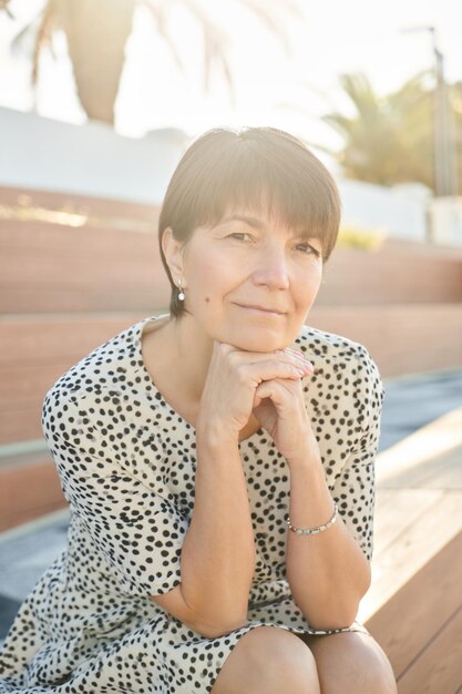 Portrait of 50 year old happy caucasian woman sitting and smiling in the park on the bench adult healthy real lady