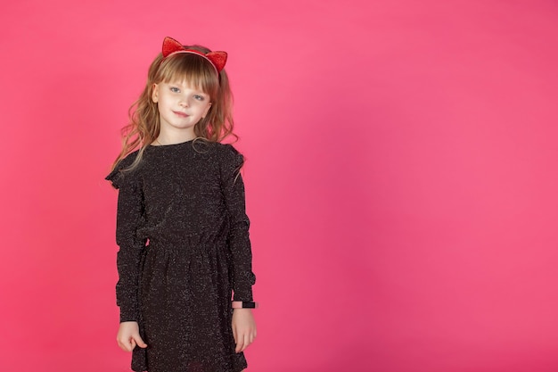 Photo portrait 6-7 year old girl in black dress on pink isolated background looks at camera