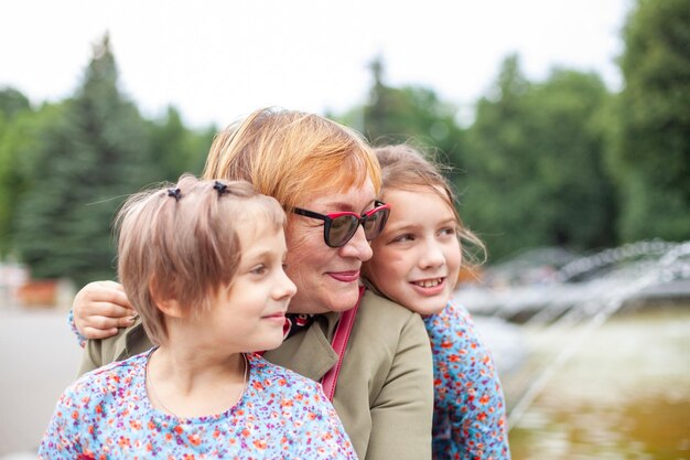 Portrait of 65yearold woman with granddaughters on background of fountain in parkxDxA