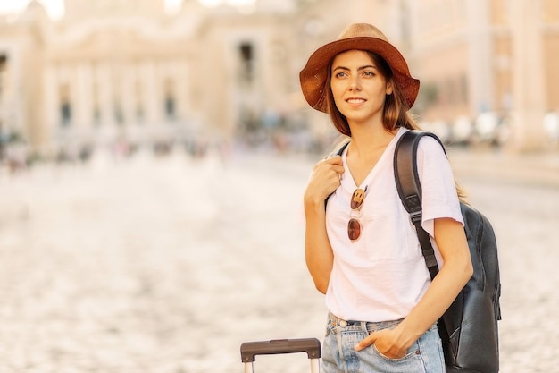 写真 バックパックを背負って帽子をかぶった女性旅行者の肖像画イタリアのローマ市の広場を見ています