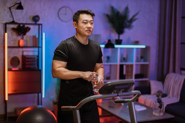 Photo portrait of active asian sportive man in black sportswear opening water bottle training at home