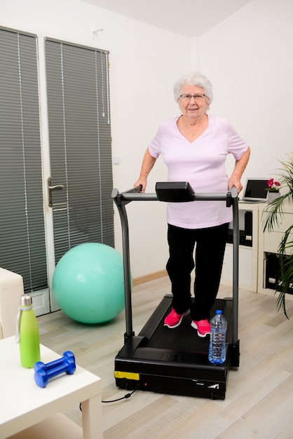 Ritratto di una donna anziana attiva e dinamica che fa fitness sportivo a casa camminando sul tapis roulant