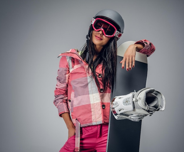 Portrait of active female in a pink ski costume holding a snowboard. Isolated on grey background.