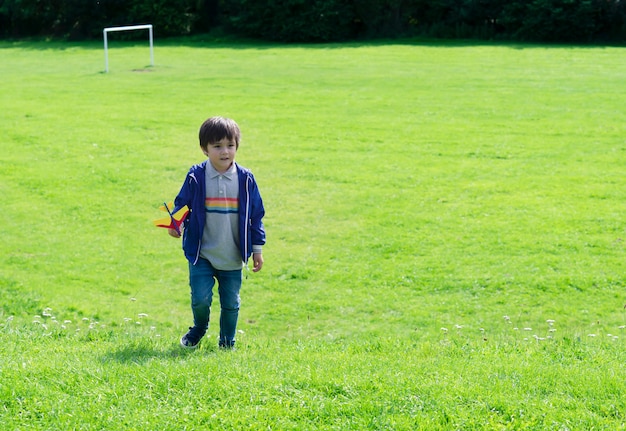 Portrait active little boy playing with toy airplane against green nature