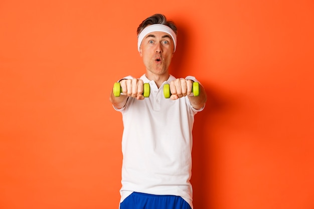 Portrait of active middle aged fitness guy, doing sport exercises with dumbbells