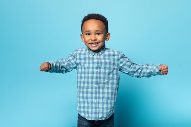 Portrait of adorable african american boy in casual clothes smiling at camera standing over studio wall free space