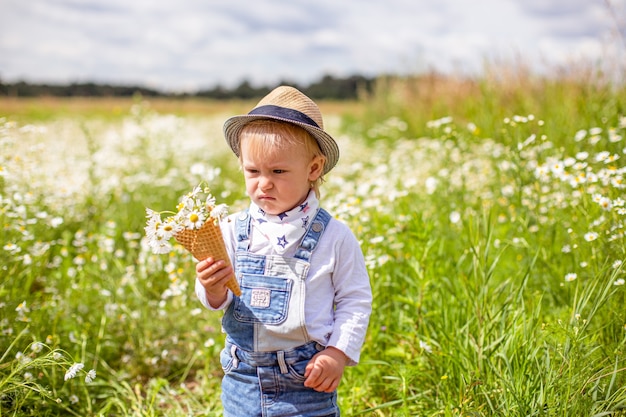 Portrait of adorable baby with flowers in chamomile field holding a bouquet of flowers