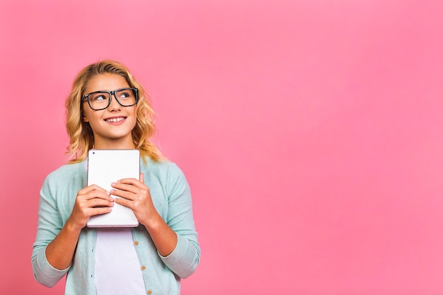 Portrait of adorable blonde kid using digital tablet device, isolated over pink background.