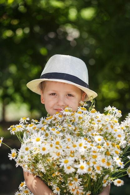 Portrait adorable boy in a hat with big white bouquet of camomiles 