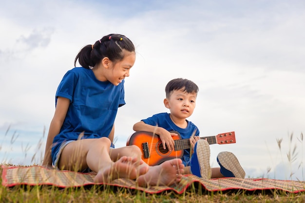 屋外で遊ぶ愛らしい兄と妹の肖像画 庭で歌を歌うアジアの子供たち 幸せな男の子と女の子がギターで屋外で楽しんで