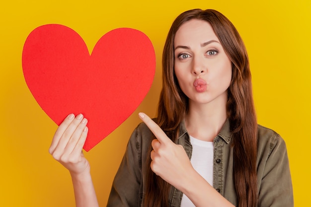 Portrait of adorable girl hold heart figure direct finger lips blow air kiss on yellow background