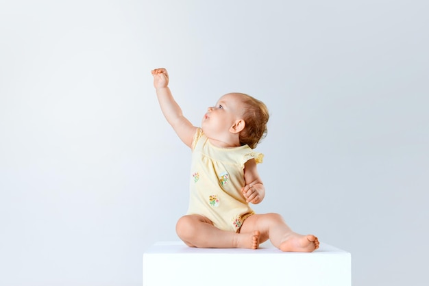 Portrait of adorable little baby girl toddler child calmly sitting and playing against grey studio