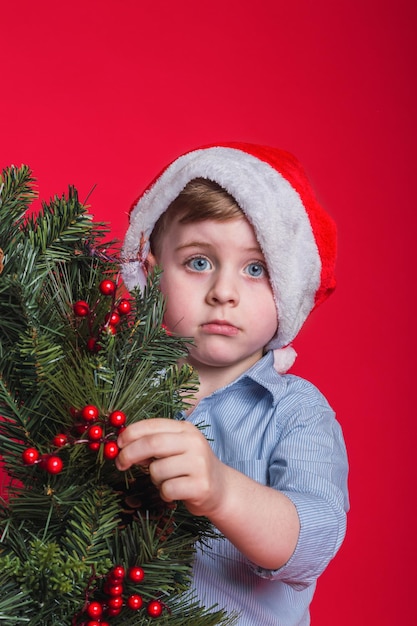 Ritratto di un adorabile ragazzino che indossa un cappello di natale su uno sfondo rosso.