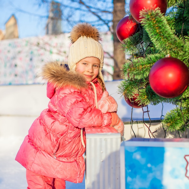 Ritratto della bambina adorabile all'albero di natale sulla pista di pattinaggio