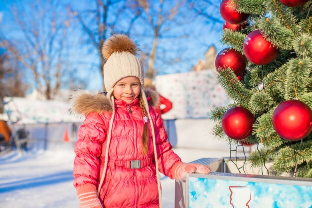 Portrait of adorable little girl near Christmas tree on skating rink