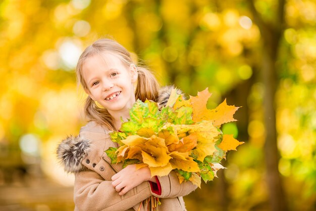 Portrait of adorable little girl with yellow leaves bouquet in fall at beautiful autumn day