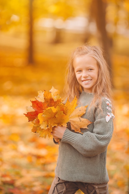 Портрет очаровательной маленькой девочки с букетом желтых листьев осенью