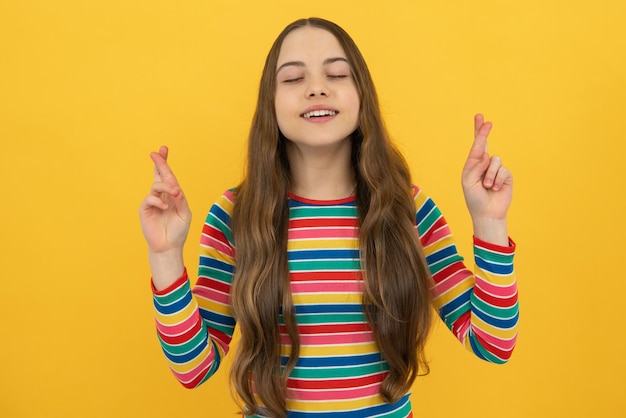 Portrait of adorable little teenager gitl standing with closed eyes and crossing fingers wishing for good luck Childhood dreams and hopes