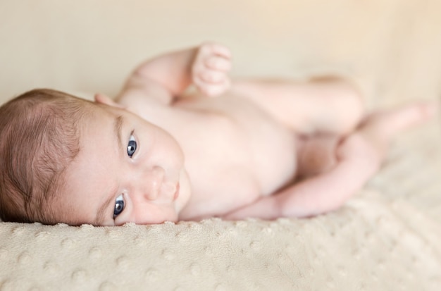 Portrait of adorable newborn baby boy with open eyes lying down over a blanket