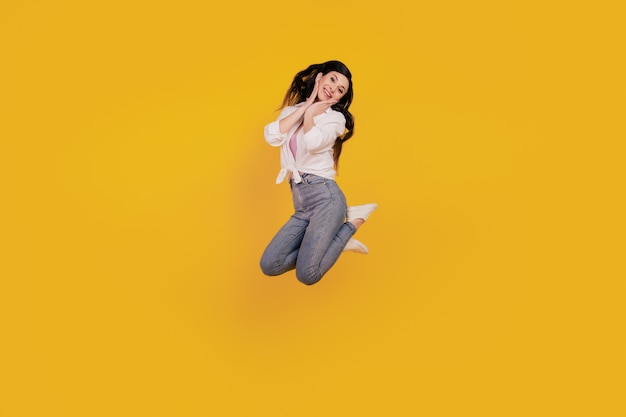 Portrait of adorable positive girl jump posing on yellow background