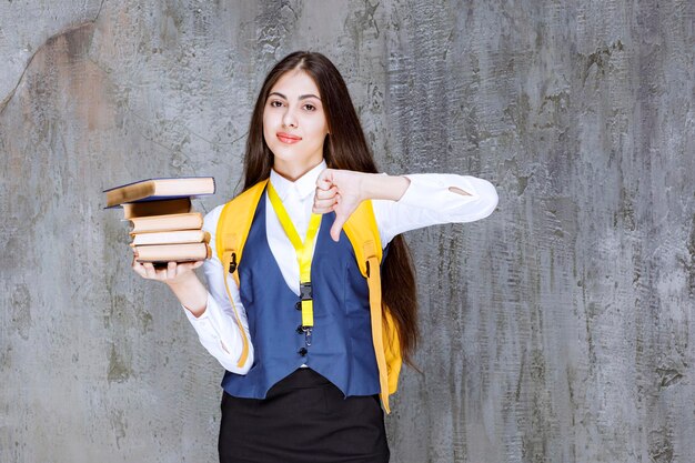 Ritratto di uno studente adorabile con uno zaino che tiene libri e dà i pollici verso il basso. foto di alta qualità