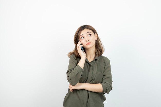 Ritratto di donna adorabile che comunica tramite cellulare sopra bianco.