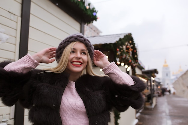 Portrait of adorable young woman wearing knitted hat and fur coat. Space for text