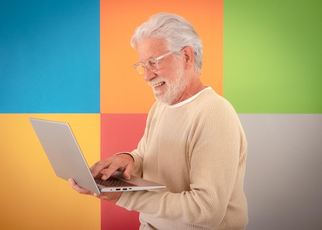 Photo portrait of adult bearded senior man holding using laptop computer standing over cute colorful background 70 years old grandfather wearing eyeglasses enjoying technology and social