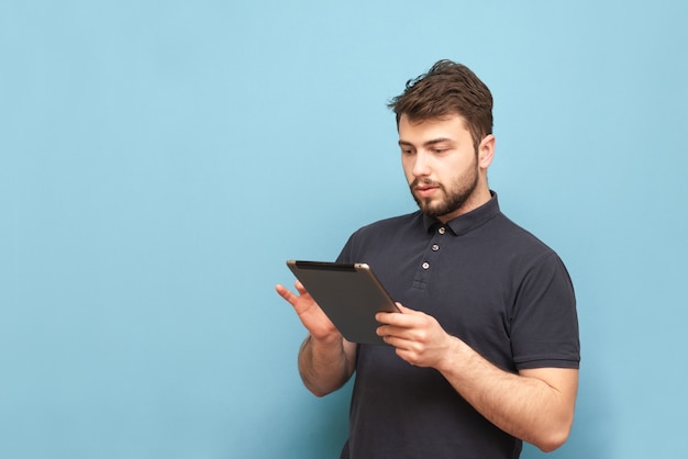 Portrait of an adult concentrated man uses the internet on a tablet, wearing a beard and a dark T-shirt.