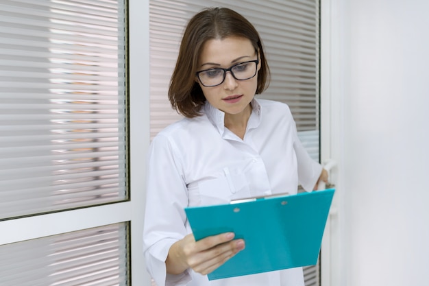 Portrait of adult female nurse, woman with clipboard, working in hospital.