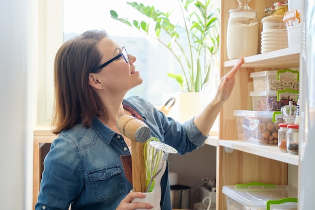 Portrait of adult smiling woman with cooking accessories in kitchen interior