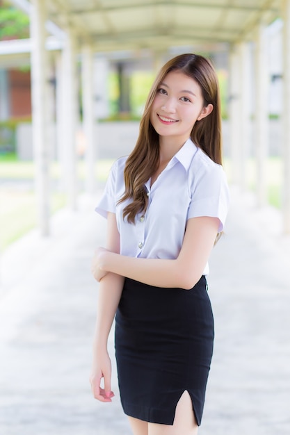 Portrait of an adult Thai student in university student uniform Asian beautiful young girl standing