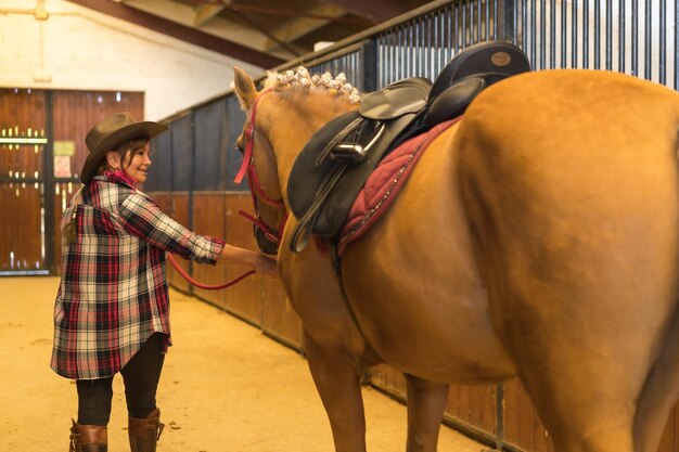 Portrait of an adult woman in a horse stable walking a brown horse, dressed in south american outfits