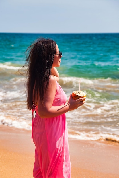 Portrait adult woman in pink beachwear and sunglasses with coconut