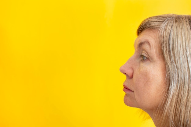 Portrait of an adult woman, standing in profile. Natural look. On a yellow background. Place for your text. Copy space