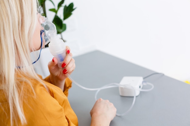 Portrait of adult woman using steam vapor inhaler nebulizer doing aerosol inhalation medicine treatment at home or hospital flu and asthma bronchitis virus healing