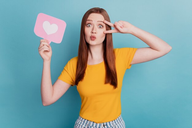 Portrait of affectionate lady hold like notification v-sign cover eye blow air kiss on blue background