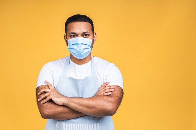 Portrait of african american black indian chef or cook with mask for coronavirus prevention isolated over yellow background whit copy space.