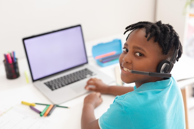 Portrait of african american boy wearing headset at desk using laptop for online school lesson