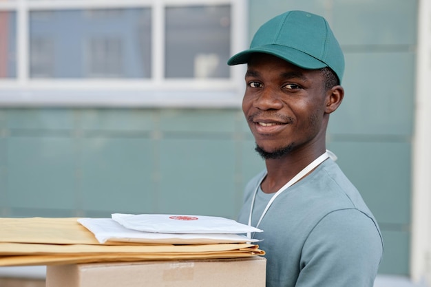 Portrait of african american delivery worker holding box and\
smiling at camera