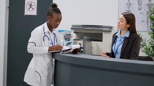 Portrait of african american doctor analyzing medical report
papers with receptionist at hospital reception counter. health
specialist working at registration desk in lobby, healthcare
appointments.