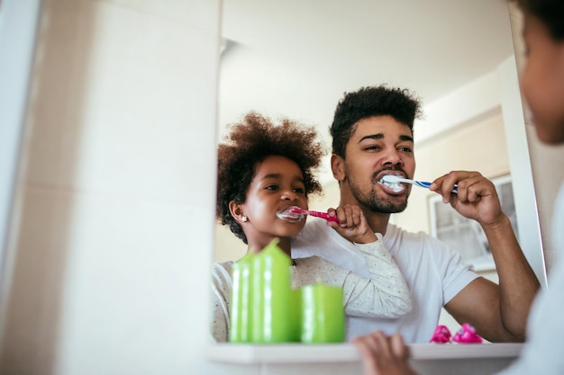 Портрет афроамериканского отца и дочери, чистящих зубы в ванной