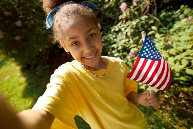 屋外のカメラに微笑むアメリカの国旗を持つアフリカ系アメリカ人の女の子の肖像画