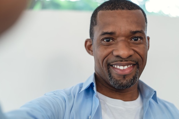 Portrait of African American handsome man smiling friendly aking selfie of himself in their living room at home People man lifestyle concept