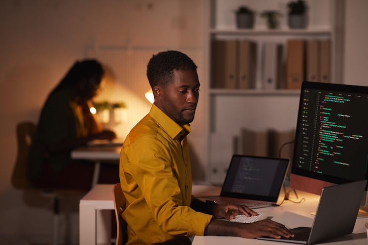 Photo portrait of african-american it developer writing code on multiple computer screens while working late in office, copy space