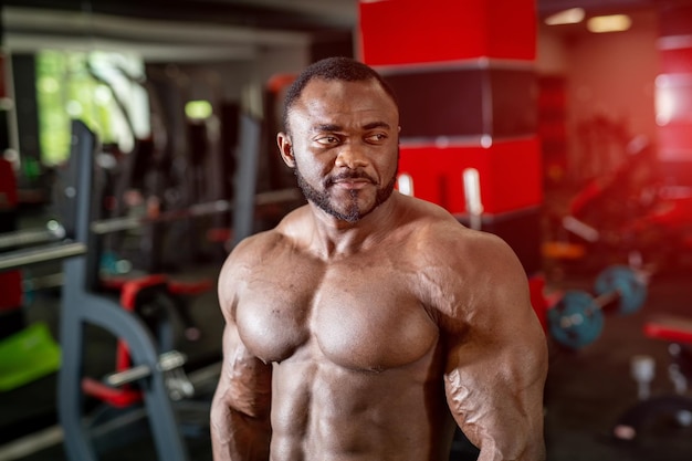 Portrait of african american male fitness trainer Bodybuilder showing his biceps and looking at the side of the gym background