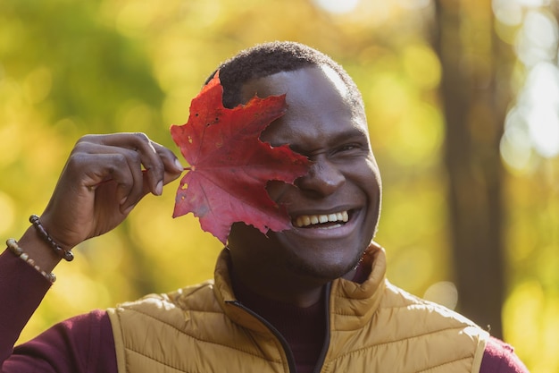 Photo portrait of african american man covering his face with autumn maple leaf autumn nature seasonal fall fashion